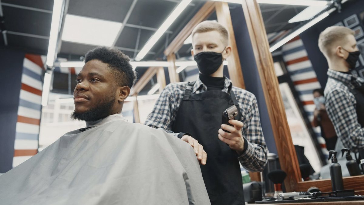Barbero repasando los laterales con máquina a un cliente sentado en la silla