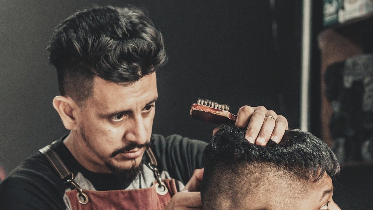 Barbero repasando un degradado en los laterales con peine y máquina